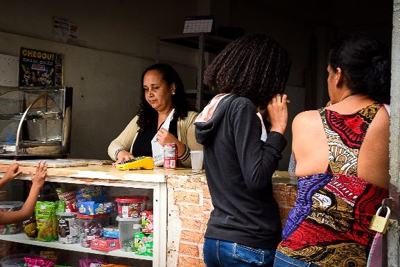 Mulher em sua pequena venda na periferia, ponto de encontro da comunidade.